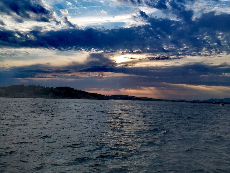 Mer agitée sous un ciel nuageux avec des collines sombres à l'horizon et une lumière tamisée au crépuscule.