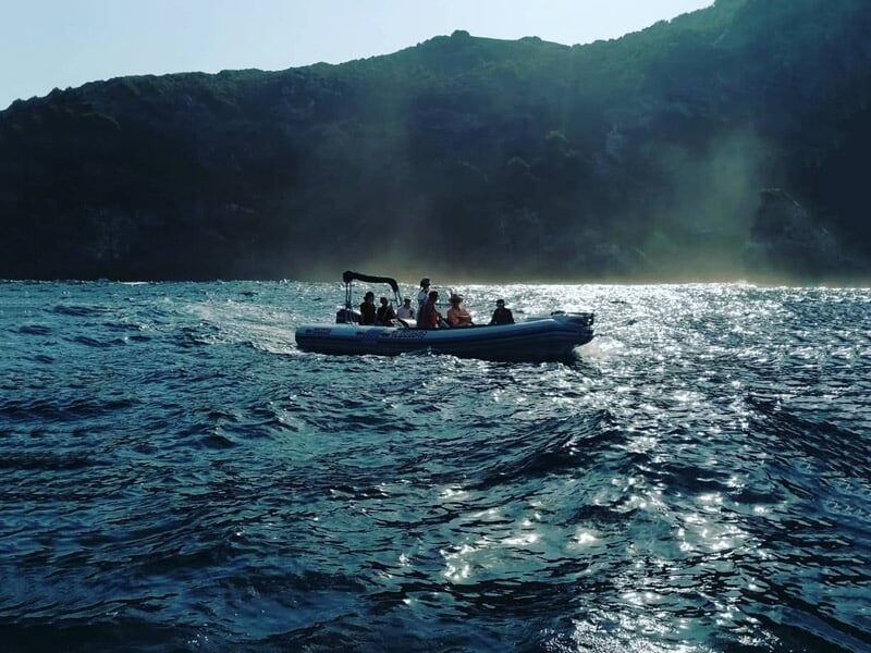 Bateau pneumatique avec plusieurs passagers naviguant sur une mer agitée près d'une côte boisée sous un ciel clair.