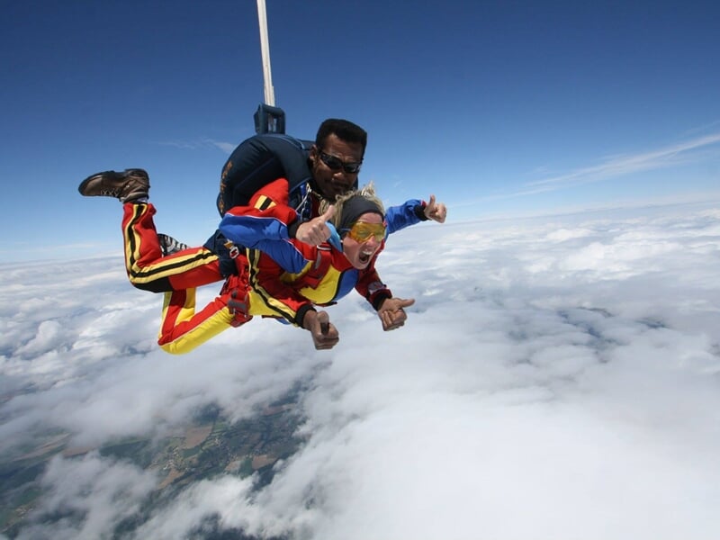 Parachutistes en chute libre au-dessus des nuages avec expressions de joie et ciel partiellement nuageux.