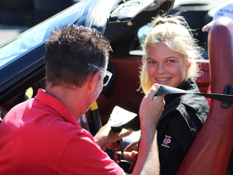 Instructeur attachant la ceinture de sécurité d'une jeune fille blonde souriante dans une voiture de sport cabriolet.