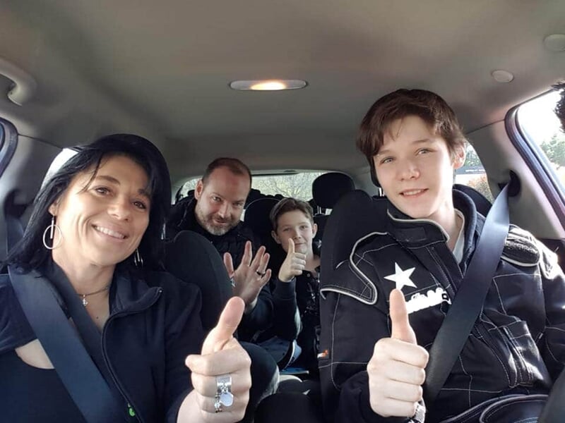 Famille de quatre personnes dans une voiture, tous souriant et levant le pouce.