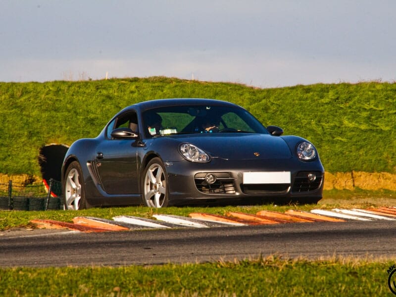 Porsche grise sur un circuit automobile avec herbe en arrière-plan. Voiture en mouvement sur une bordure de piste.