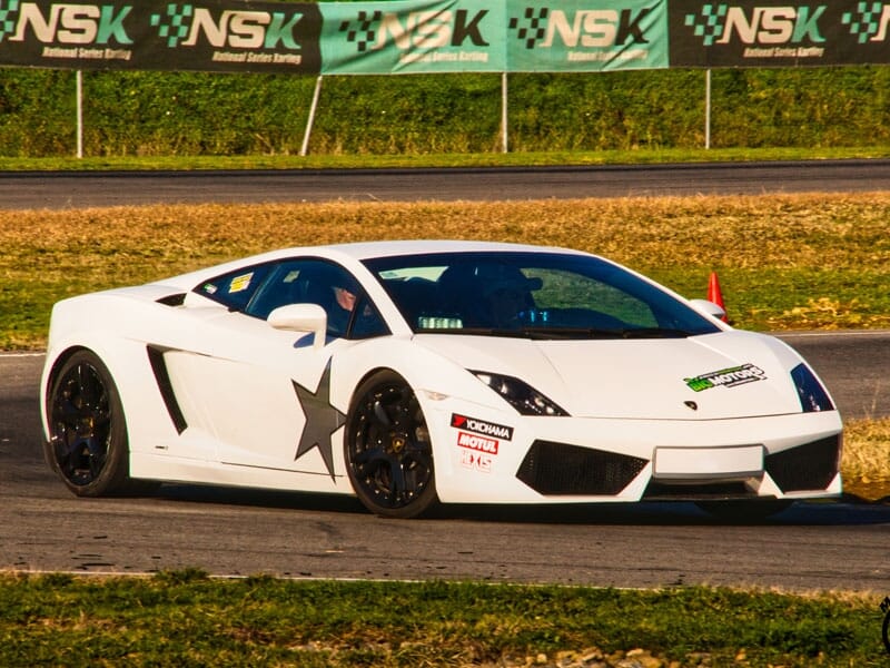 Lamborghini Gallardo blanche avec une étoile noire sur la portière. Publicités pour Motul et Yokohama sur le capot. Circuit automobile avec bannière NSK en arrière-plan.