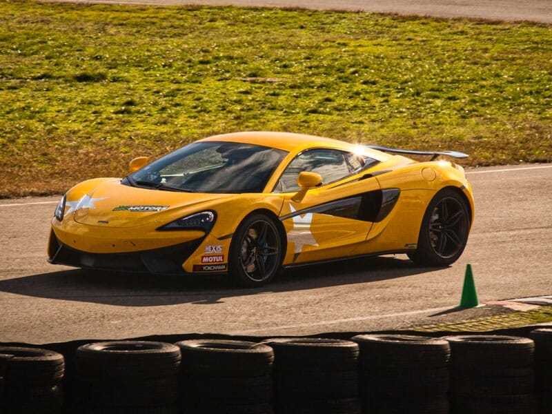 McLaren jaune avec des étoiles blanches sur les portières. Publicités pour Big Motors, Motul et Yokohama. Circuit automobile avec herbe en arrière-plan.