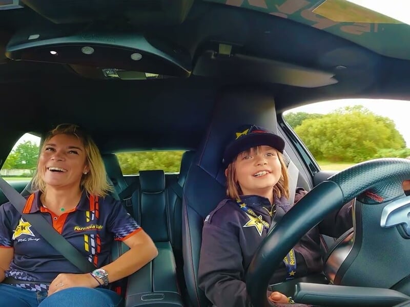 Un enfant souriant au volant d'une voiture de course avec une instructrice à ses côtés lors d'un stage de pilotage.