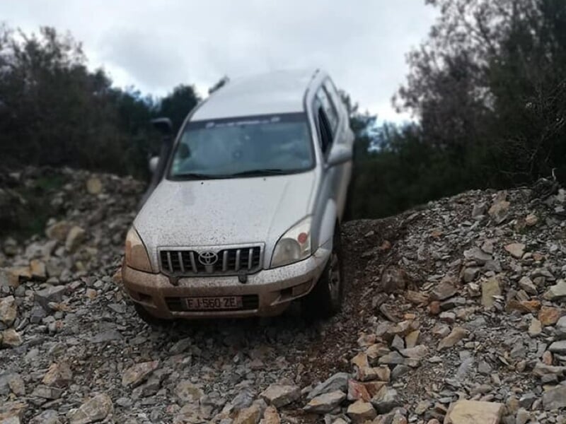 Véhicule 4x4 gris descendant un chemin rocheux escarpé en milieu naturel boisé.