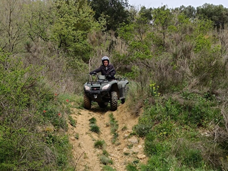 Homme en quad tout-terrain noir descendant une pente escarpée, entouré de végétation luxuriante et de buissons verts.