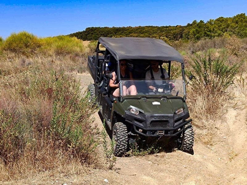 Groupe de personnes dans un quad tout-terrain avançant sur un chemin accidenté bordé de broussailles et de petites plantes.
