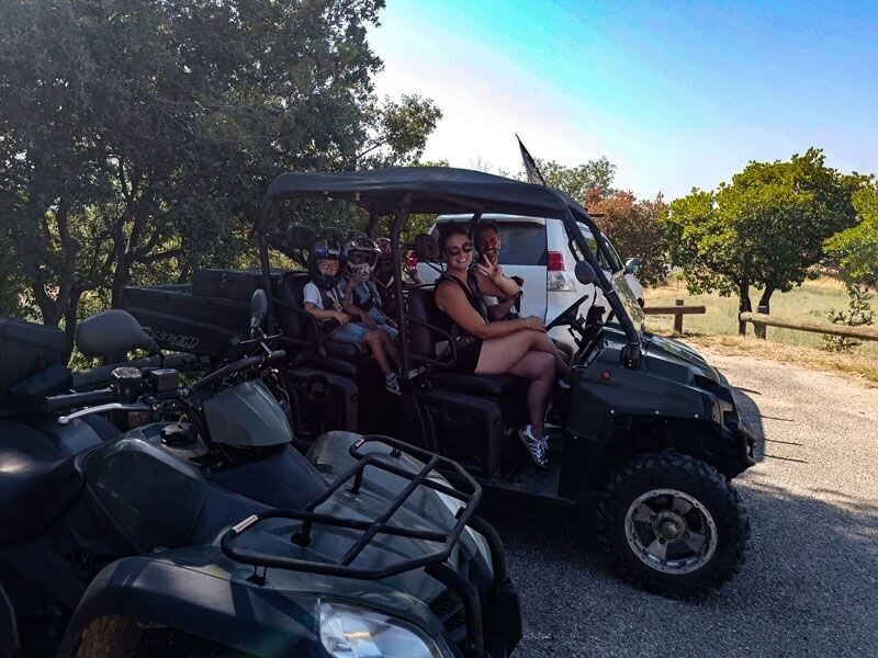 Famille posant dans un quad tout-terrain stationné sur une route goudronnée avec des arbres et un véhicule blanc en arrière-plan.