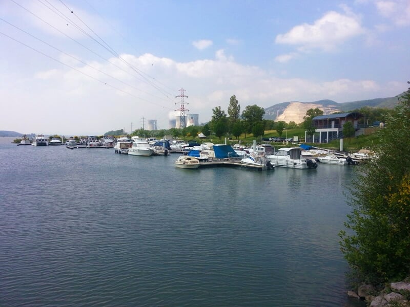 Vue panoramique d'un port de plaisance avec plusieurs bateaux amarrés sur une étendue d'eau entourée de verdure.