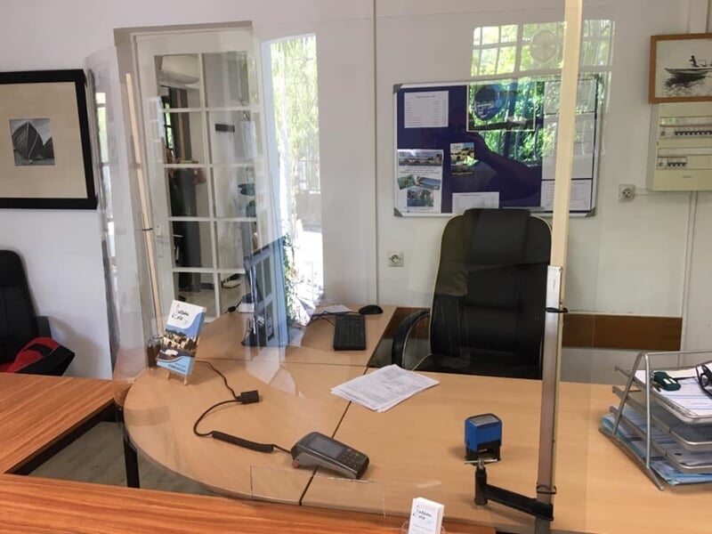 Bureau d'accueil avec un fauteuil noir, un bureau en bois et une protection en plexiglas transparente.