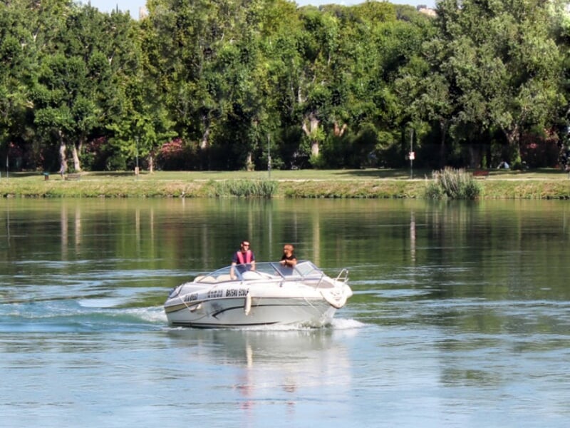 Deux personnes naviguent sur un petit bateau blanc sur une rivière calme entourée d'arbres verts.