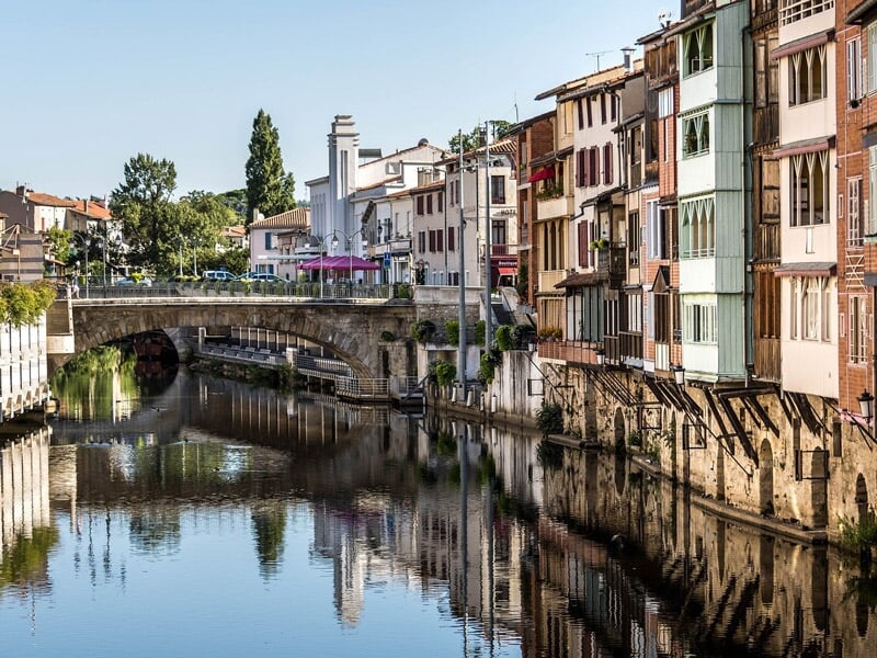 Vue d'une rivière calme bordée de maisons colorées et d'un pont en pierre sous un ciel clair
