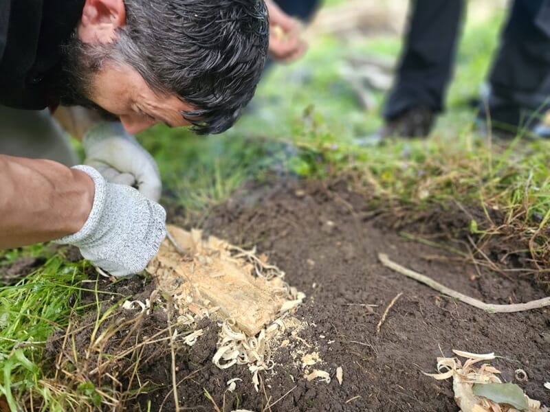 Homme concentré utilisant un outil en bois pour frotter et créer du feu dans un environnement naturel vert.