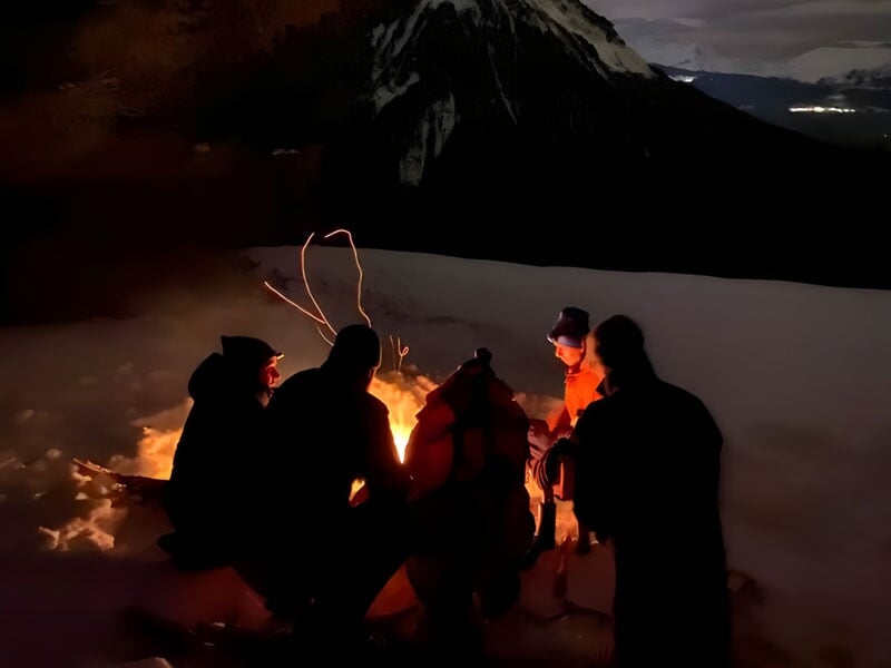 un groupe d'aventuriers dînent autour d'un feu de camp dans la neige