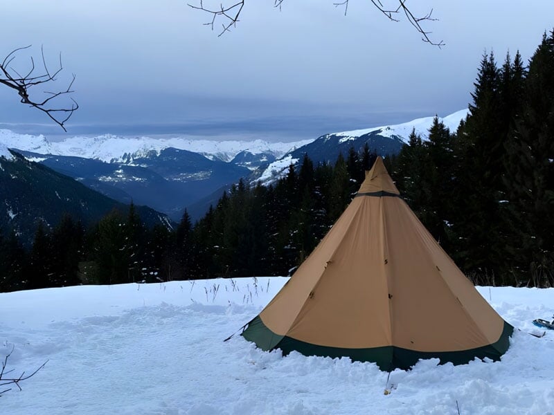 un tipi se dresse sur la neige devant une vallée