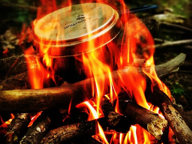 Casserole sur un feu de camp vibrant, cuisant sur des bûches enflammées