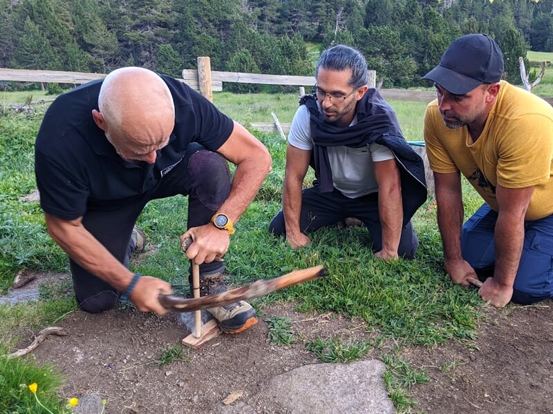 Trois hommes apprenant à faire du feu dans la nature avec un bâton et une planche en bois