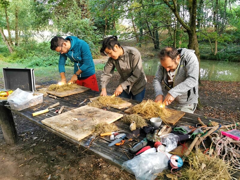 Groupe de personnes pratiquant des techniques de survie, allumant un feu sur une table en bois en plein air