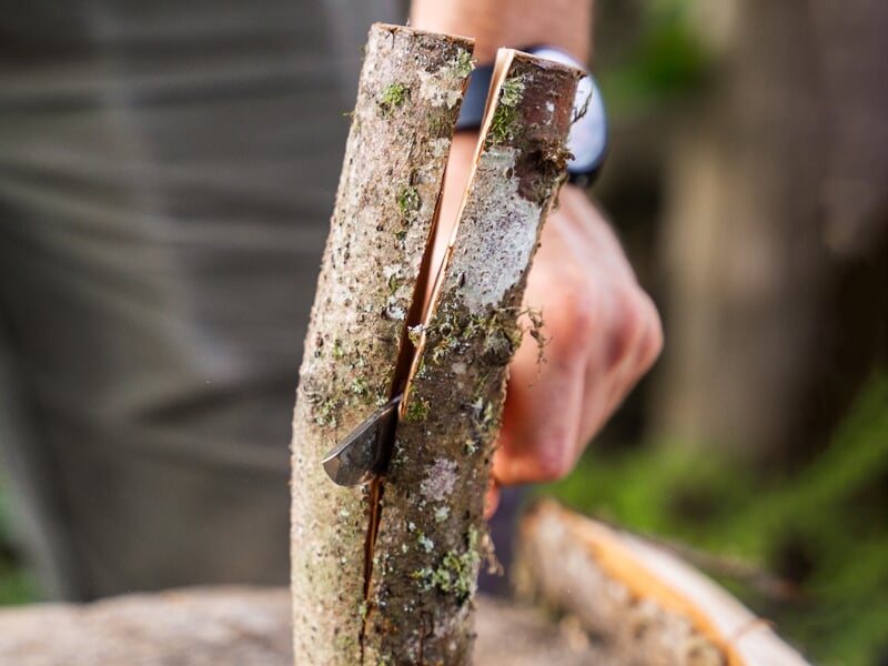 Gros plan d'une main tenant un morceau de bois contre lequel une lame est en train de couper, soulignant les activités de survie ou de bushcraft