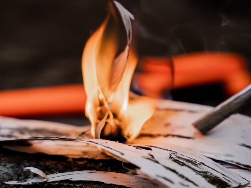 Un feu de camp en plein air avec des flammes orange et jaunes, entouré de pierres avec deux casseroles suspendues au-dessus, évoquant une cuisson sur feu de bois