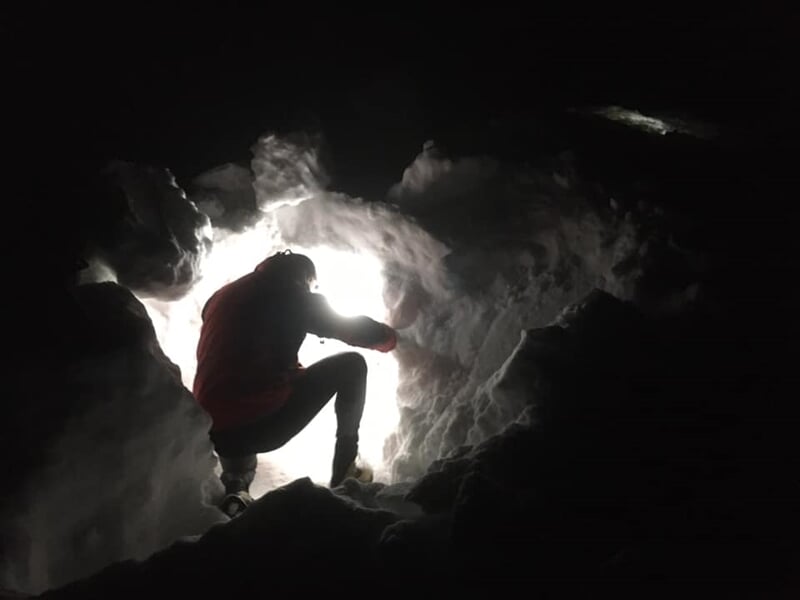 Personne à l'intérieur d'un tunnel de neige, éclairée par la lumière extérieure dans l'obscurité.
