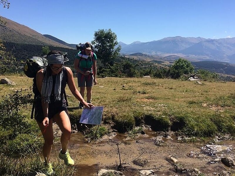 Deux randonneurs marchant sur un sentier en terrain sec, l'un tenant une carte, avec montagnes en arrière-plan.