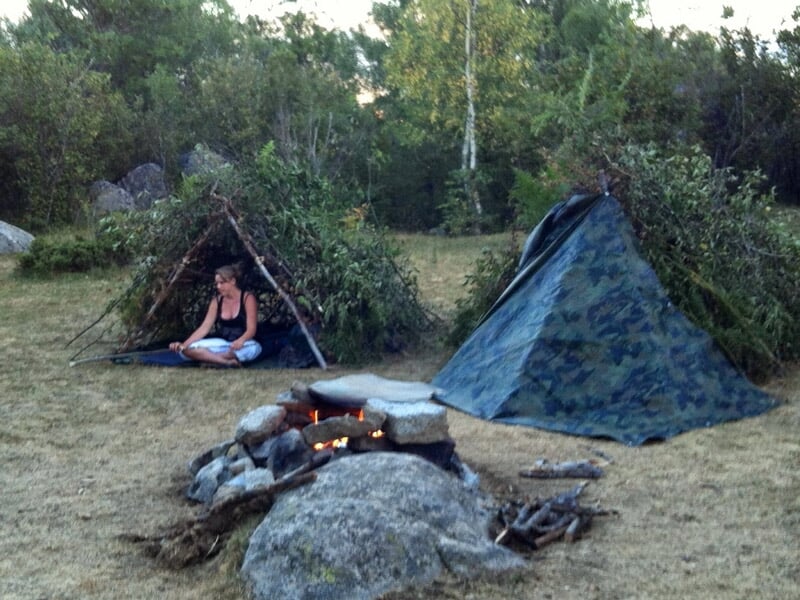 Deux abris de fortune en pleine nature, l'un en forme de tipi et l'autre en forme de tente, avec un feu de camp.