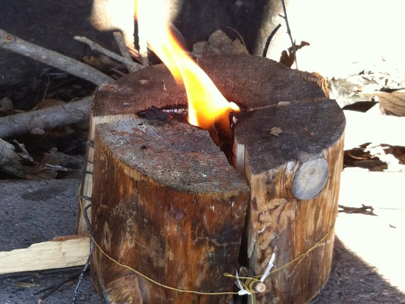 Tronc d'arbre fendu en deux avec un feu allumé au centre, utilisé comme source de chaleur en extérieur.