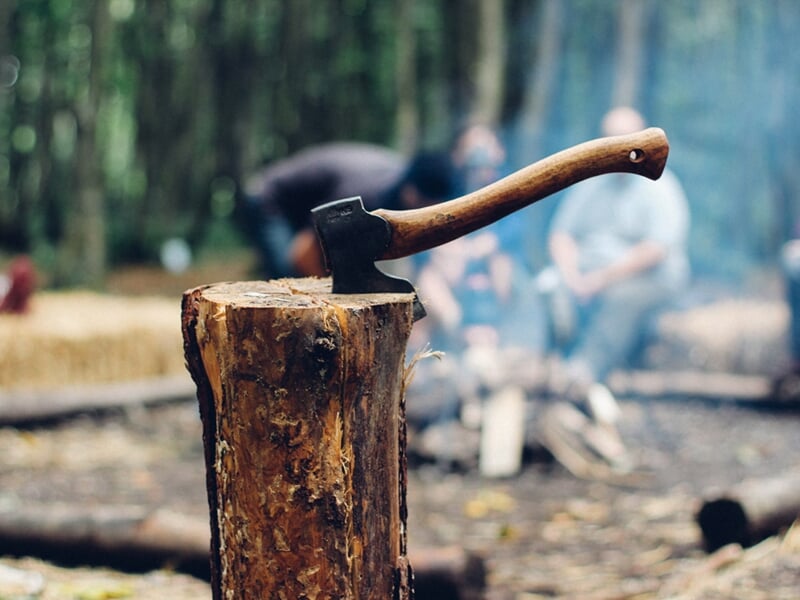 Hache plantée dans une bûche en bois au camp de survie en forêt avec des personnes en arrière-plan