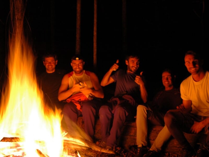 Groupe d'hommes assis autour d'un feu de camp la nuit en pleine nature, ambiance conviviale