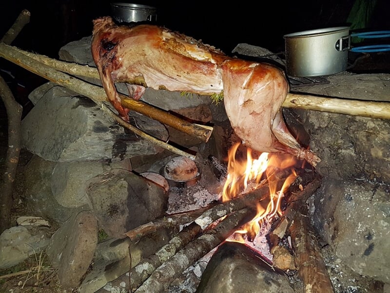 Viande en cuisson lente sur un feu de camp avec des pierres et des ustensiles de cuisine
