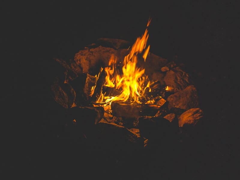 Petit feu de camp allumé dans un cercle de pierres dans un environnement sombre en pleine nature