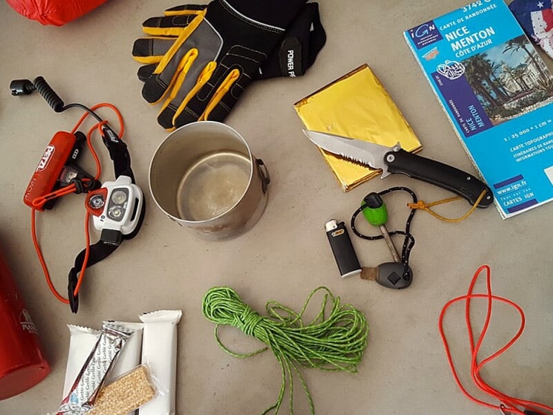 Matériel de survie étalé sur une surface, comprenant gants, corde, briquet, scie et autres outils