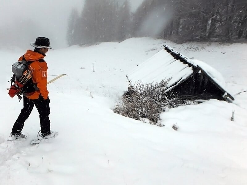 Personne en tenue de randonnée avec sac à dos marchant dans la neige près d'une cabane enneigée
