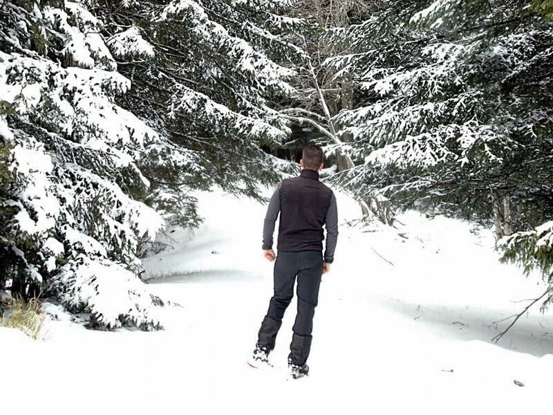 Homme marchant seul dans une forêt enneigée avec des arbres couverts de neige autour de lui