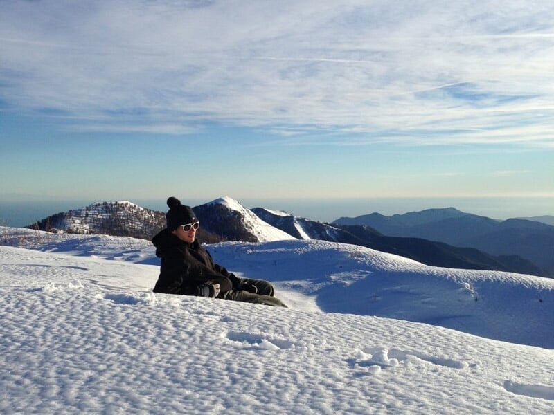 Personne assise dans la neige sur une montagne ensoleillée avec des lunettes de soleil et bonnet