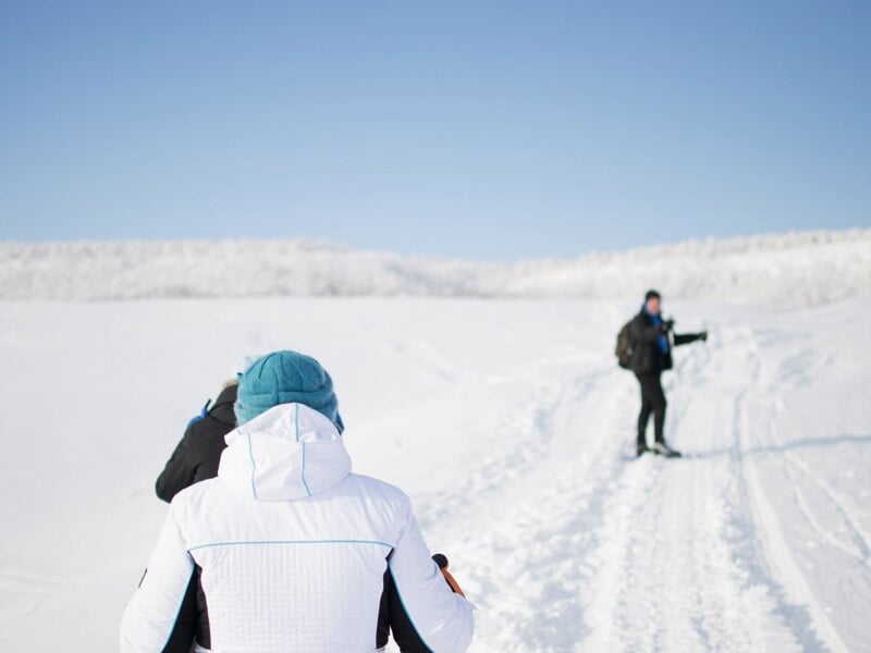 Deux personnes en tenue d'hiver marchant dans la neige avec un ciel clair et paysage blanc