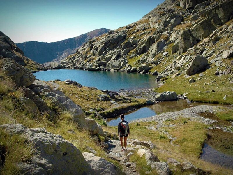 Personne marchant sur un sentier de montagne rocheux près d'un lac entouré de sommets verts