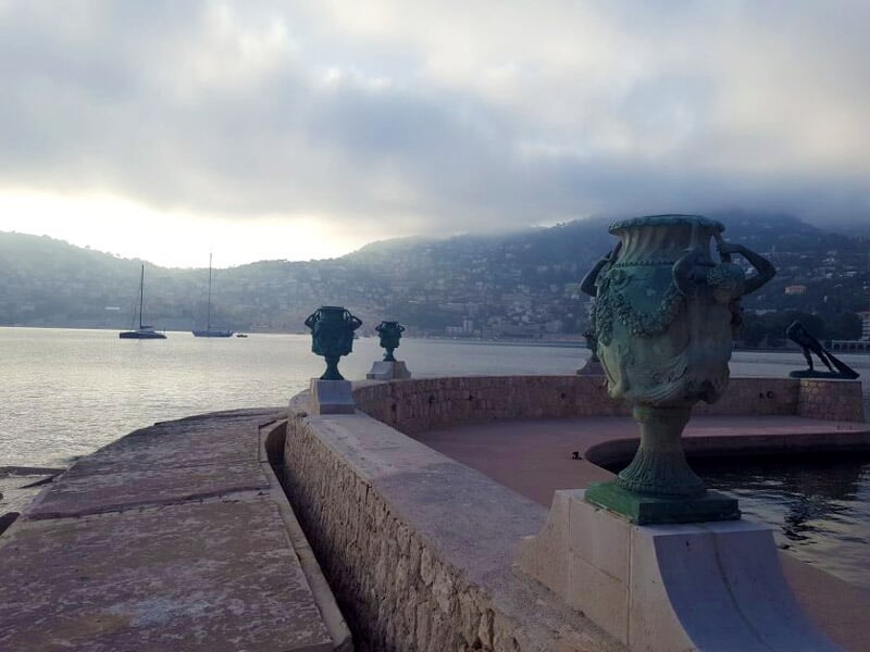 Vue sur une ville côtière avec un port, des bateaux et des collines en arrière-plan sous un ciel clair