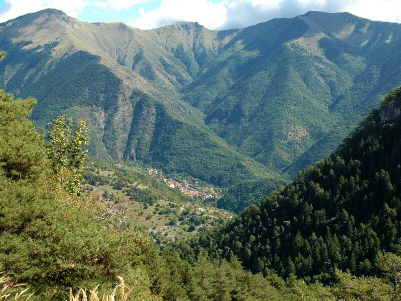Paysage de montagne verdoyante avec des forêts denses et des vallées sous un ciel partiellement nuageux