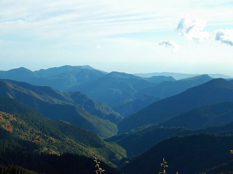 Vue sur une chaîne de montagnes avec des sommets verts et un ciel bleu clair avec quelques nuages