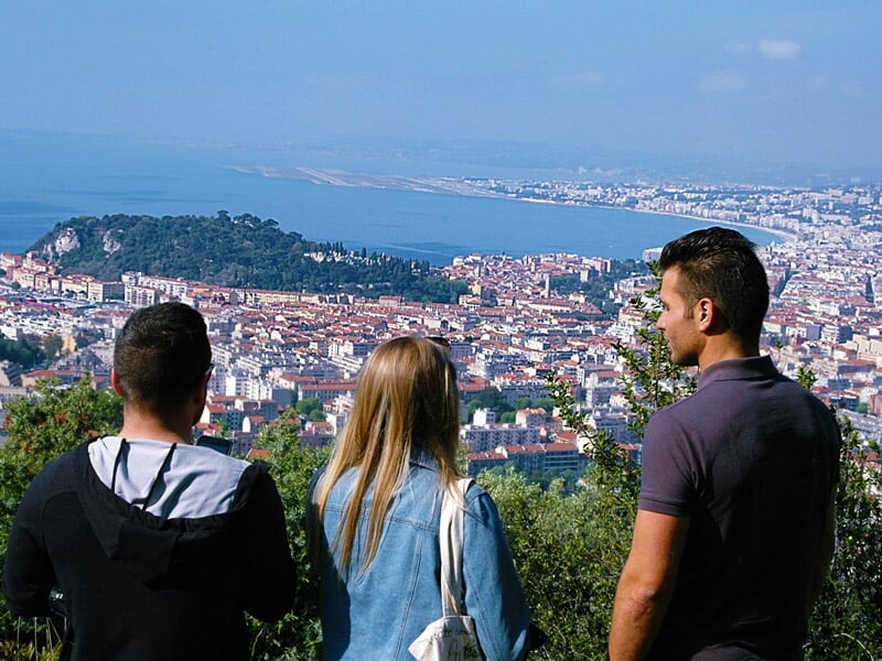 Trois personnes debout sur une colline avec vue sur une ville et la mer en arrière-plan