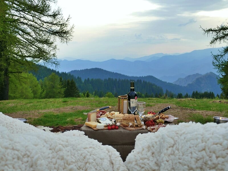 Pique-nique en montagne avec une table garnie de vin, fromage et charcuterie dans un cadre naturel