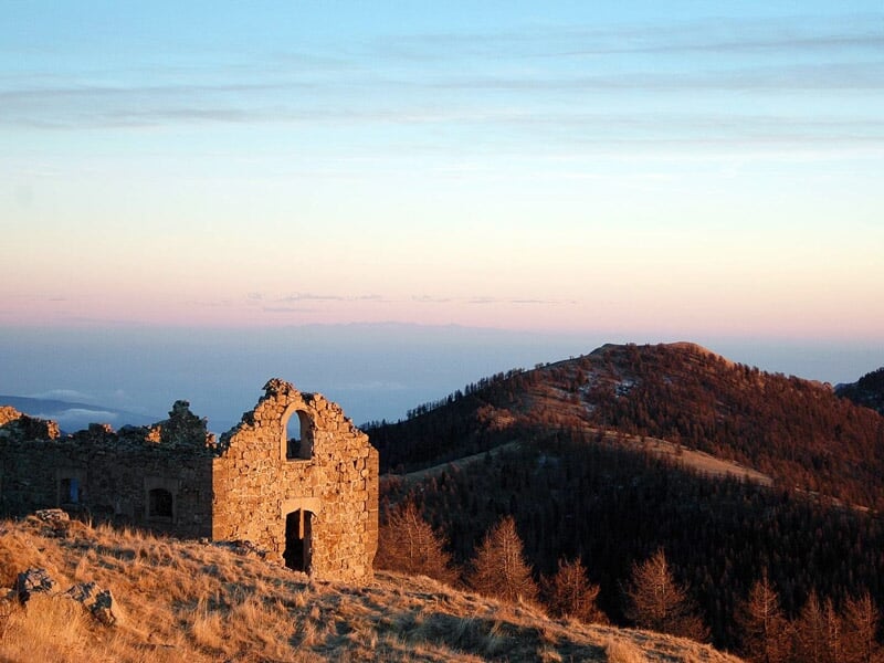 Ruines d'un ancien bâtiment en pierre éclairées par la lumière du coucher du soleil en montagne