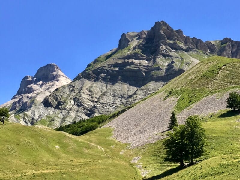 Paysage de montagne verdoyante avec un sommet rocheux imposant sous un ciel bleu clair sans nuages.