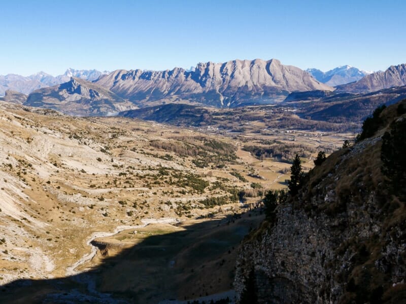 Vue d'une vallée montagneuse avec des rochers clairs et des ombres portées, sous un ciel bleu avec quelques nuages.