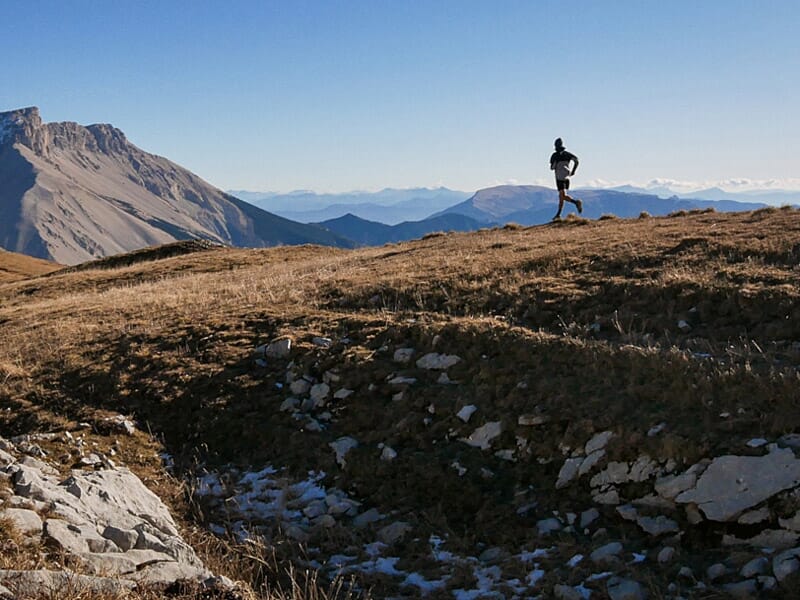 Un coureur solitaire sur un sentier de montagne au sommet d'une colline avec un panorama de montagnes au loin.