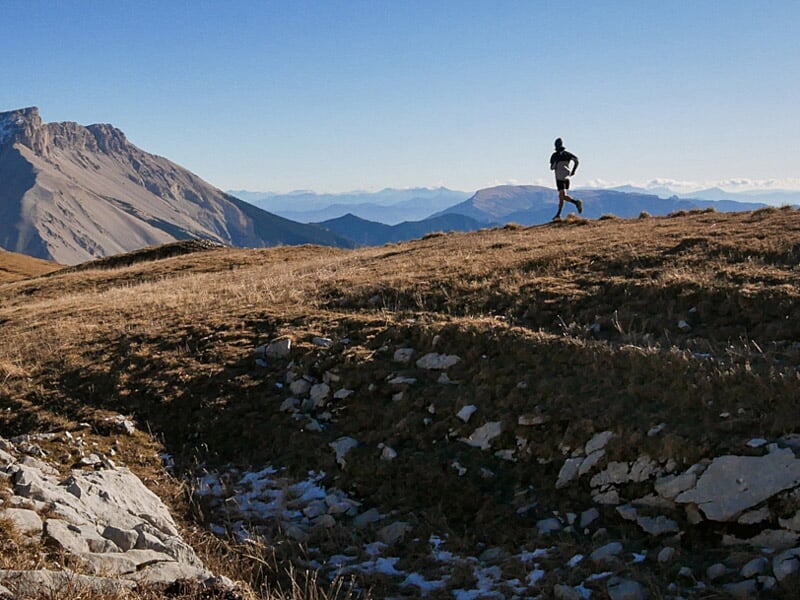 Un coureur solitaire sur un sentier de montagne au sommet d'une colline avec un panorama de montagnes au loin.