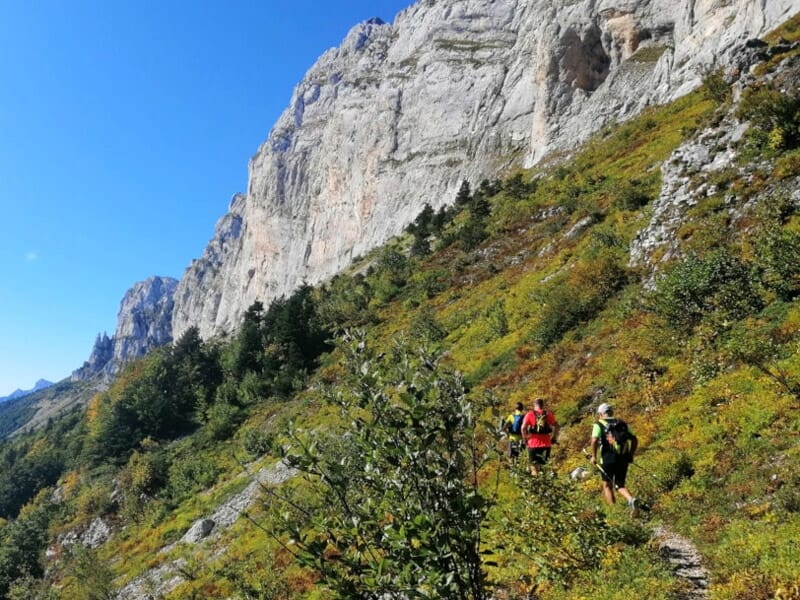 Deux coureurs de trail en montagne sur un sentier étroit entouré de végétation et de falaises rocheuses